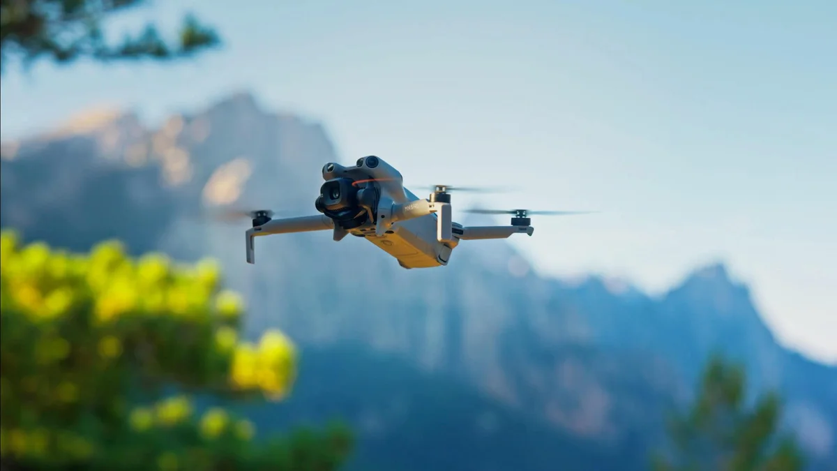Un DJI Mini 5 Pro vuela entre montañas, con un arbusto en flor delante
