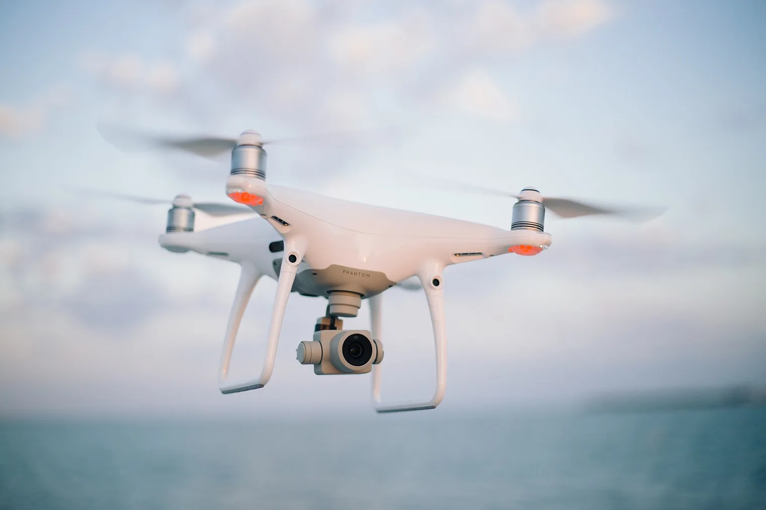 Un dron cuadricóptero blanco con cámara, volando sobre el mar al atardecer