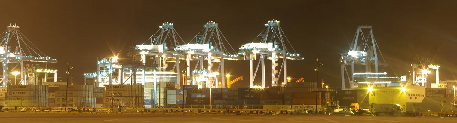 Las grúas pórtico del puerto de Algeciras iluminadas de noche, con pilas de contenedores de Maersk y CMA CGM