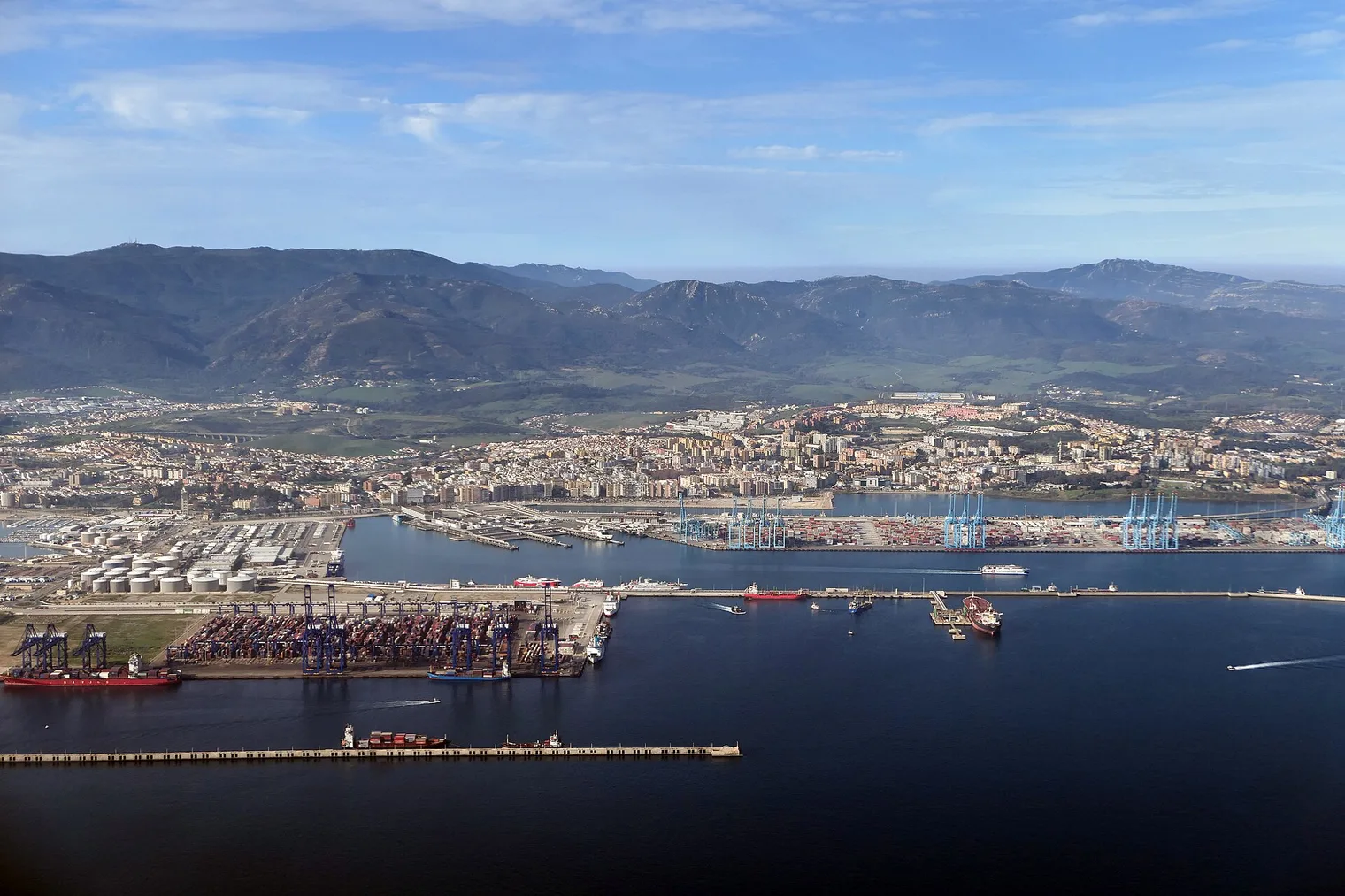 Vista aérea de la bahía de Algeciras, con las grúas azules de la terminal de contenedores, la ciudad y las montañas del Campo de Gibraltar al fondo