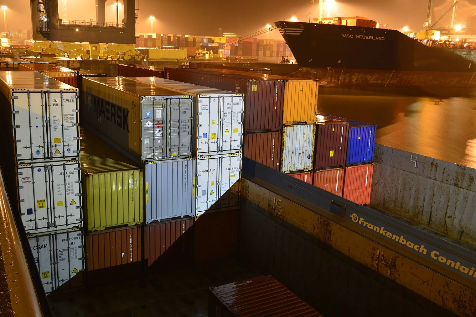 Contenedores apilados en el Deurganckdok del puerto de Amberes, de noche, con el portacontenedores MSC Nederland atracado al fondo