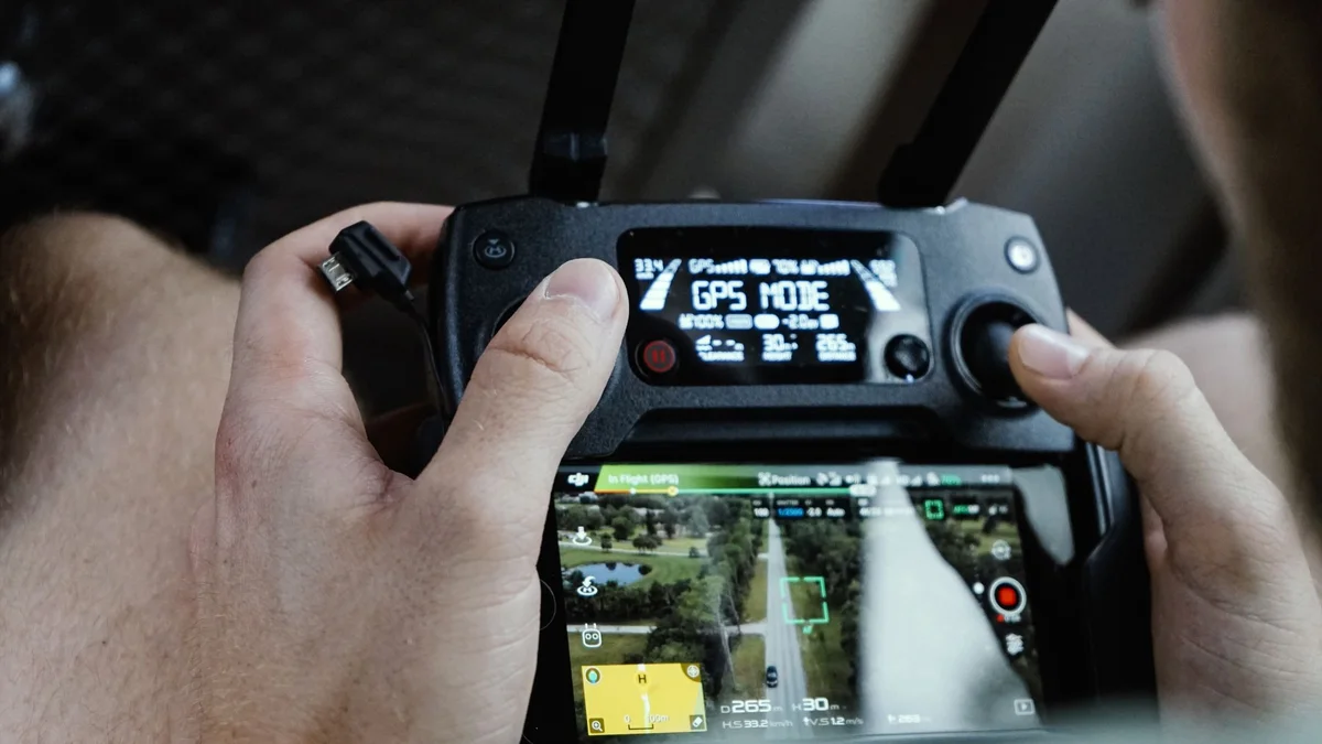 Manos de un piloto en un mando de dron cuya pantalla dice «GPS MODE»